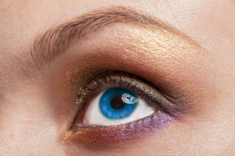Une femme applique des ombres à paupières sur ses yeux bleus