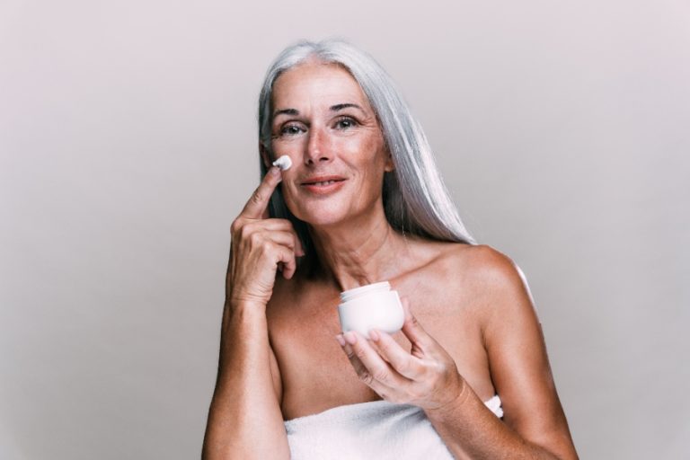 Femme appliquant une crème anti-âge sur son visage devant le miroir