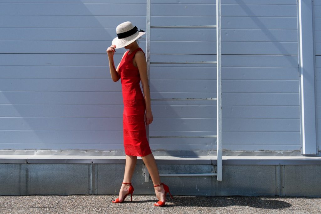 Une femme élégante avec un chapeau, une robe rouge et un talon pointu rouge