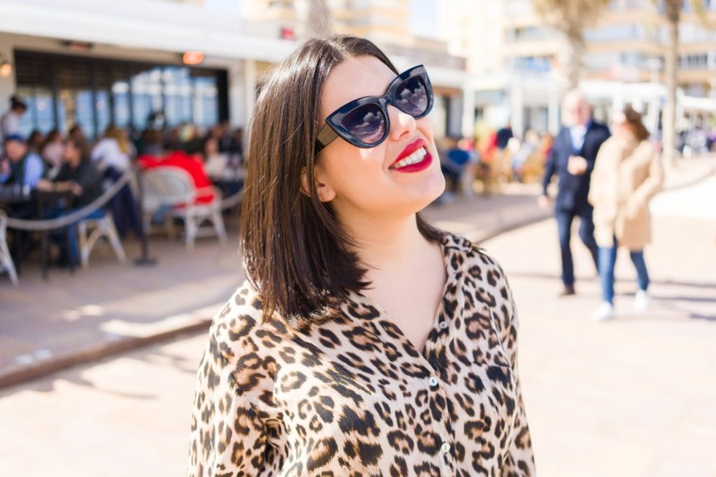 Une femme souriante avec une lunette noire et une robe léopard