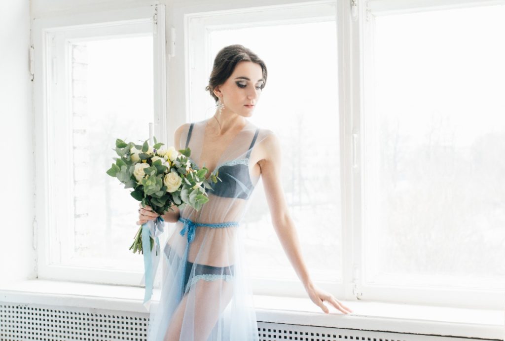 Une femme près de la fenêtre avec une robe transparente et un bouquet de fleur