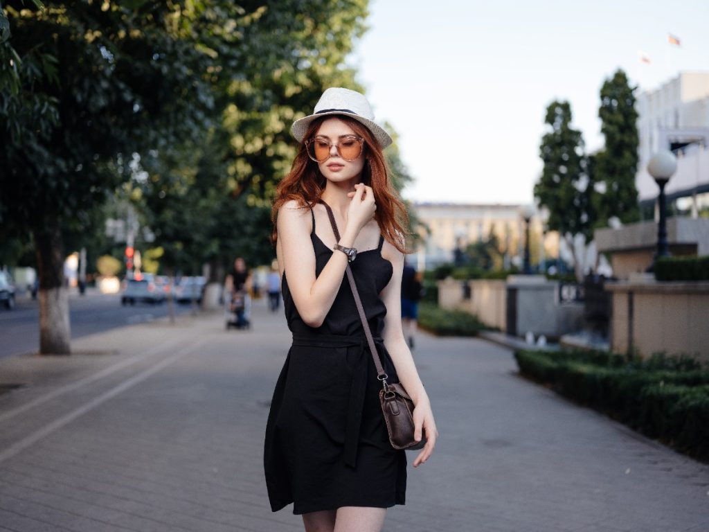 Une jolie femme habillée avec une robe noire, un chapeau et un sac