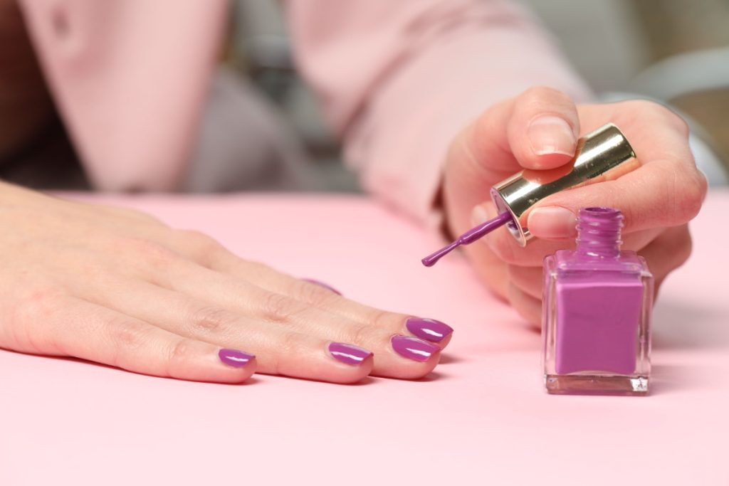 Une femme appliquant du vernis à ongle violet