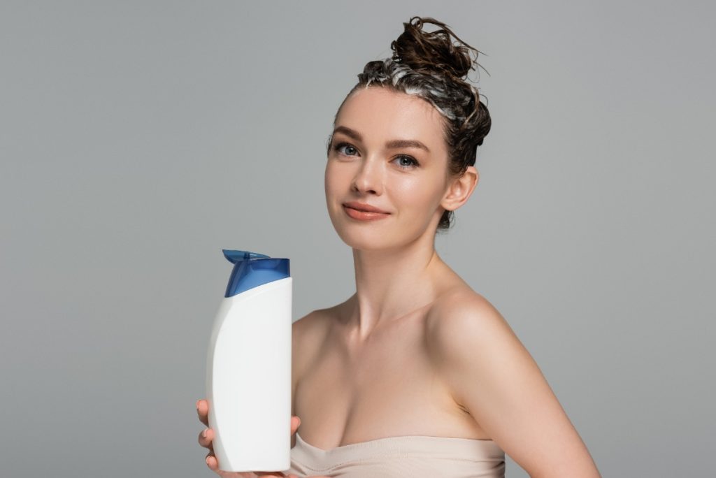 Une femme avec des cheveux mouillés tenant un flacon de shampoing