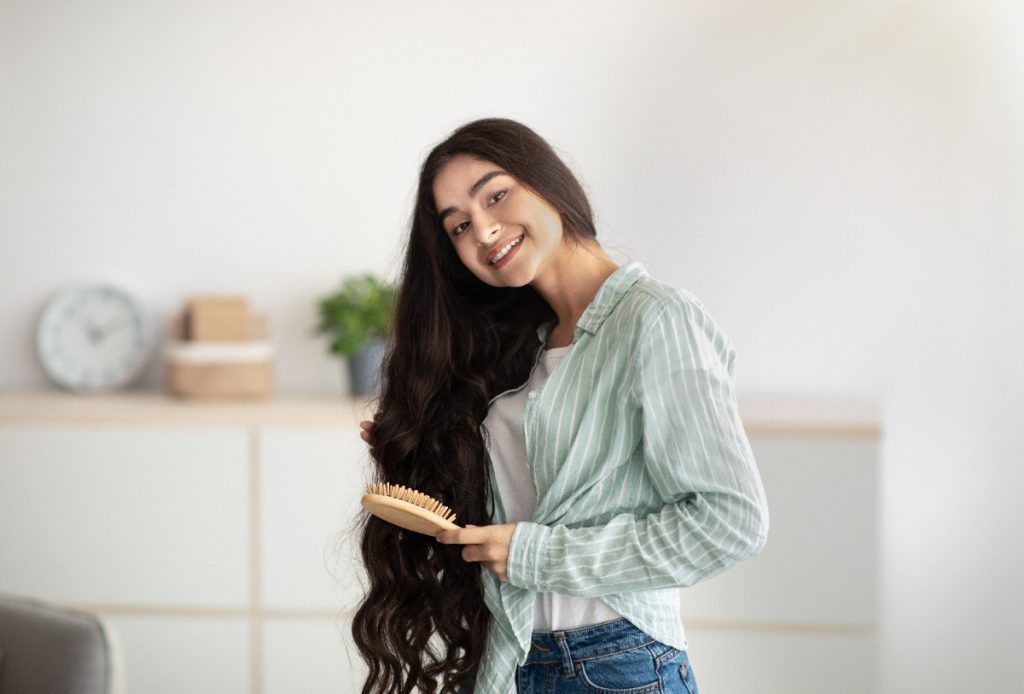 Une femme souriante se brossant ses longs cheveux