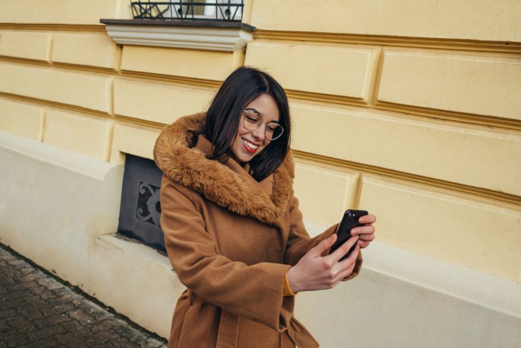 Une femme souriante portant un manteau et utilisant son téléphone